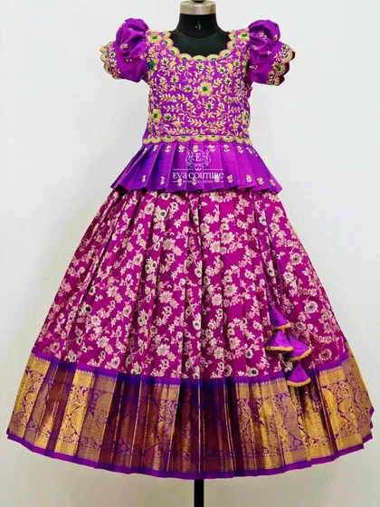 A rich purple floral brocade lehenga. The blouse is heavily embroidered and features a pleated peplum design.