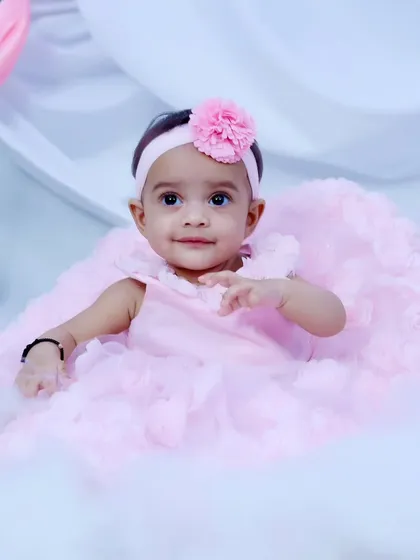 A baby girl in a light pink dress, sitting up in a sea of soft clouds for her fairy-themed shoot.