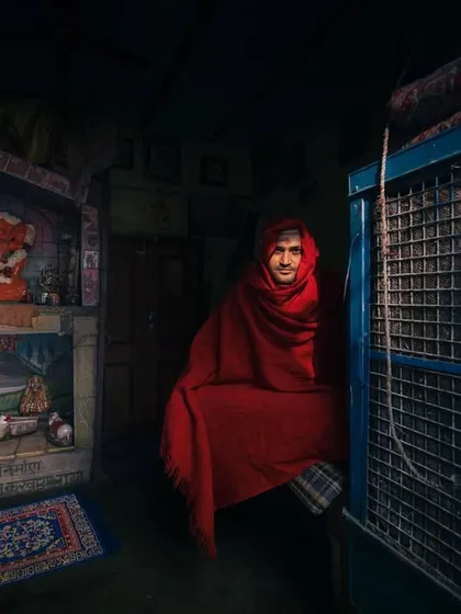 A person wrapped in a red shawl sits in a dimly lit room, the single source of light creating a dramatic and intimate "winter rays" portrait.
