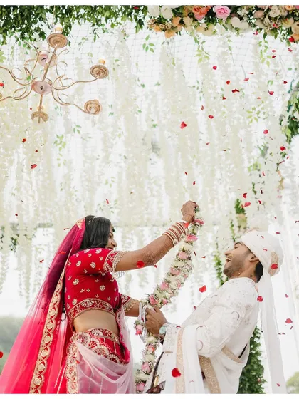 The Varmala exchange, full of joy and a shower of petals. This shot captures the peak of the action, with the bride playfully trying to garland the groom.
