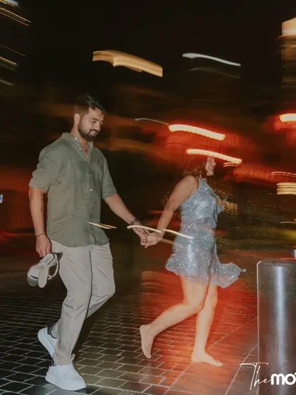 A fun, candid shot of a couple running barefoot through the streets of Dubai at night. The motion blur from the city lights adds a dynamic and energetic feel to this spontaneous moment.