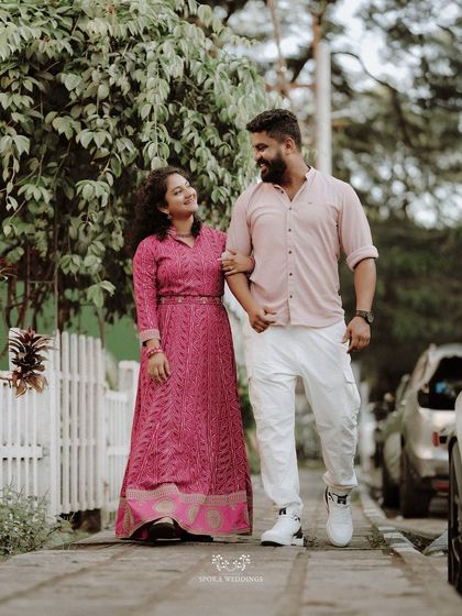 The couple taking a romantic stroll down a sidewalk lined with a white picket fence.