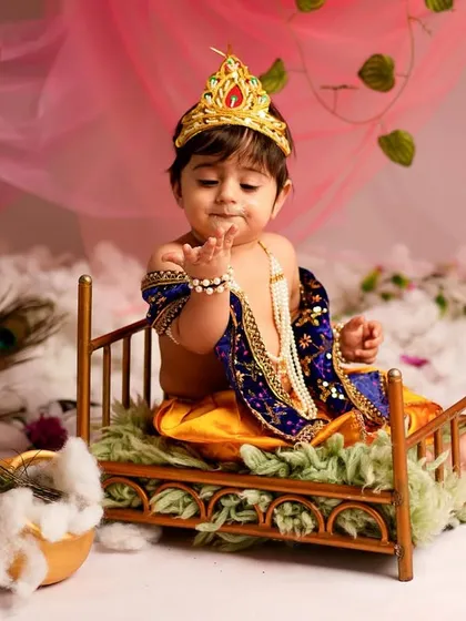 A divine pose from our little Krishna, sitting on a miniature bed. The details, from the costume to the props, are carefully chosen to create a timeless festive portrait.
