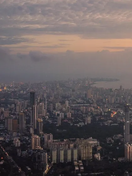 A panoramic drone shot of Mumbai under a cloudy, moody sky, capturing the vastness of the city and its coastline.