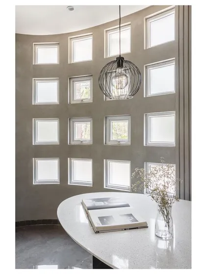 Inside the 'House Under Tabebuia Trees', this dining nook is defined by a curved wall with a grid of small windows. Our guiding principle here was 'If Light defines a space, Colours define sense'. The design manipulates natural light to create a serene, almost surreal experience for the inhabitants.
