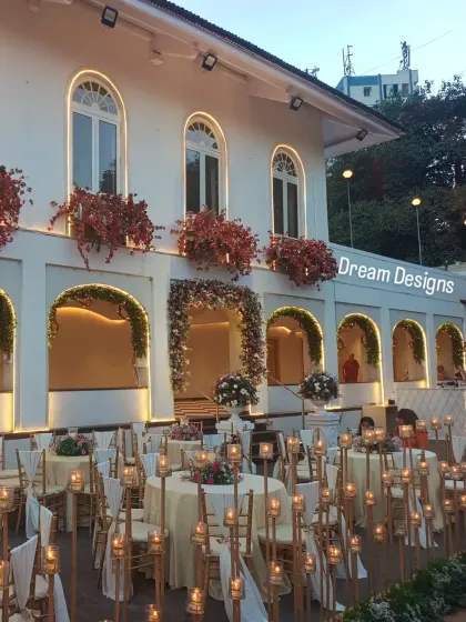 A wide view showing the candle-lit aisle in the context of the venue's beautiful facade. The combination of architectural lighting and candlelight creates a layered and sophisticated look.