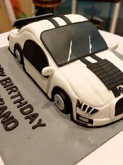 A sleek, white sports car cake with black racing stripes. This 3D sculpted car cake is a popular choice for husbands' birthdays and car enthusiasts.