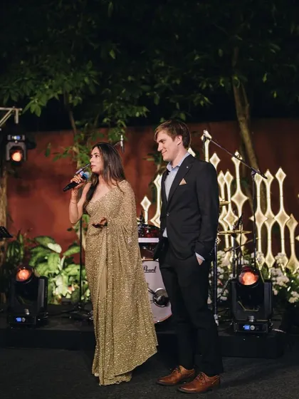 The happy couple addressing their guests. Styling a couple means ensuring their outfits work together on stage and off. His simple, well-fitted suit allows her glamorous saree to be the star.