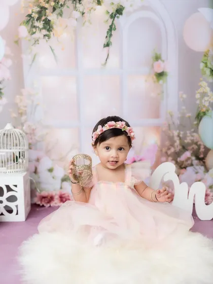 A classic first birthday portrait, complete with a "One" sign and a beautiful, soft backdrop.