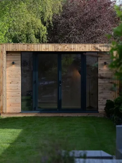 An outdoor tiny prefabricated house with wood cladding and a large glass sliding door. This compact structure can serve as a garden room, a studio, or a guest cabin.