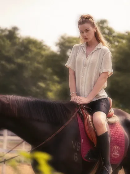 A soft, dreamy photograph of a model on horseback, with a lush, green background. The lighting and composition give this image a serene and timeless quality.