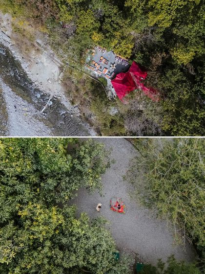 An aerial drone shot capturing the scale of a vibrant Mehendi setup nestled by the river at The Den, Corbett, surrounded by the dense jungle.