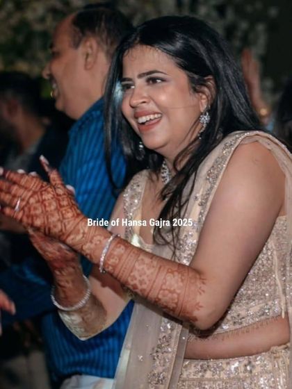 A bride clapping with joy during her wedding festivities. Her smile is radiant, and her mehendi adds to the celebratory and happy atmosphere.
