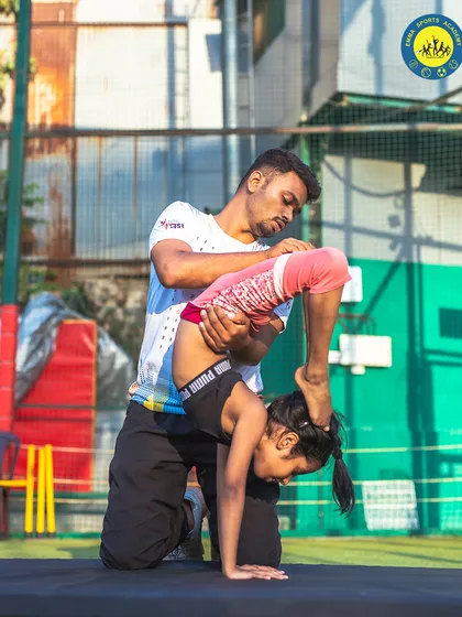 A coach assists a young gymnast with a scorpion stretch, helping her improve flexibility and control.