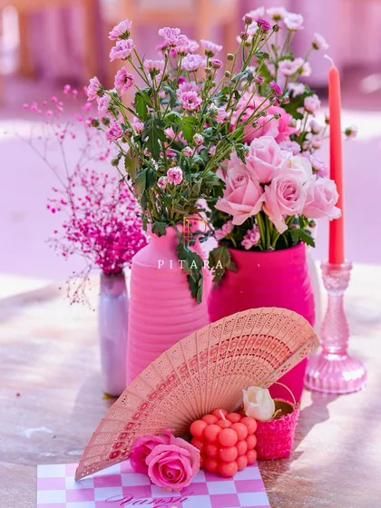 A charming detail shot featuring a vintage-style hand fan, a bubble candle, and delicate florals in pink vases. Every element is chosen to contribute to the overall romantic and whimsical mood.