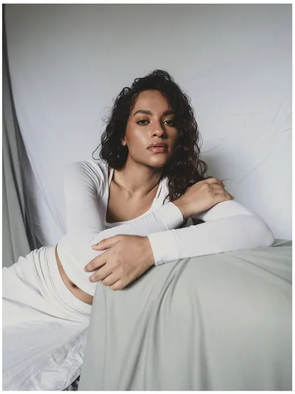 Another shot from the minimal all-white series. The model's direct gaze creates a strong connection with the viewer, contrasting with the soft, dreamy quality of the overall setup.
