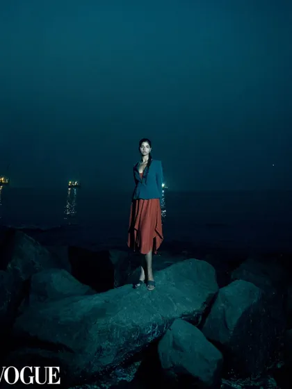 A wide, atmospheric shot taken at dusk, which was featured in PhotoVogue. The image uses a flash to illuminate the model against the deep blue of the sea and sky, creating a cinematic and lonely beauty.