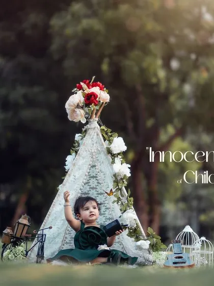 Innocence unveils the beauty of childhood. A little girl in a dark green dress holds a camera, ready to capture her own memories in this outdoor teepee setup.
