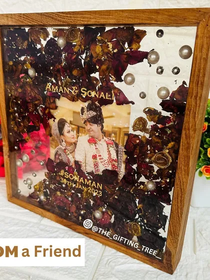 A 10x10 inch square teakwood frame with a beautiful arrangement of preserved red and yellow flowers around a central wedding photo.