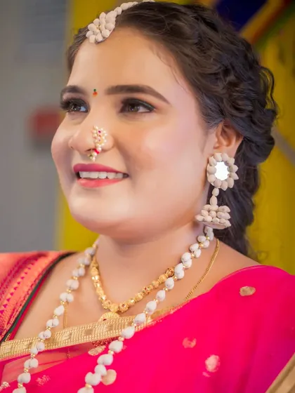 A close-up portrait of a bride, showcasing her beautiful smile and traditional jewelry. This shot focuses on her expressive face and the fine details of her Maharashtrian bridal look, including her nath and earrings.