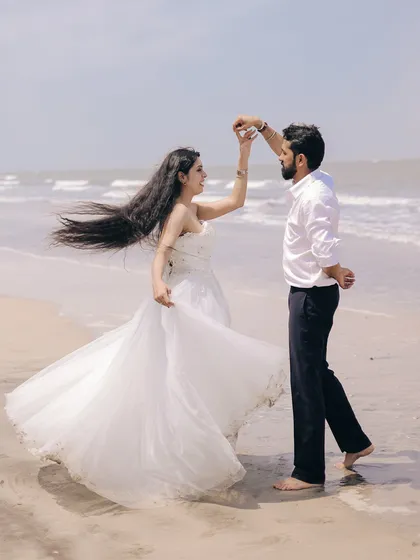 A joyful, dynamic shot of a couple dancing on the beach for their pre-wedding shoot. The bride's flowing white dress and the ocean backdrop make for a stunning, lively image.