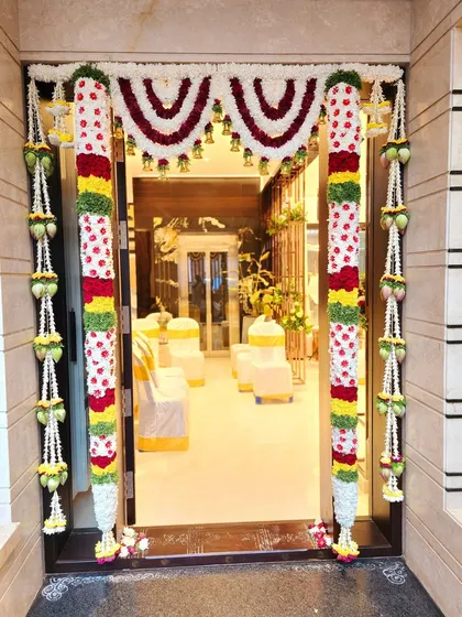 A beautifully decorated main door sets the tone for the entire celebration. For this housewarming, I used intricate flower columns and a traditional *thorana* with hanging bells to welcome guests into the new home.
