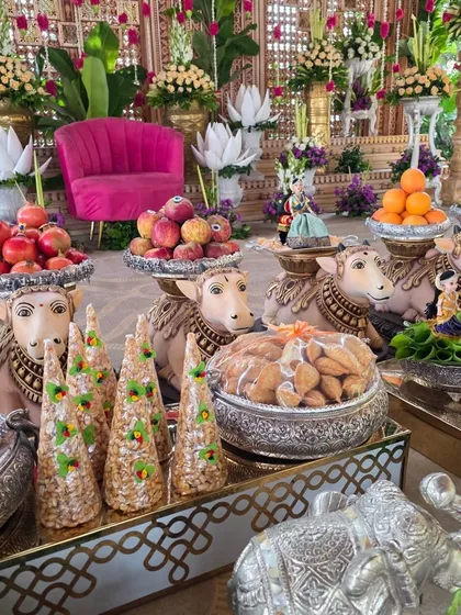 A close-up showcasing the detailed plate and prop arrangements I provide. This display includes decorated cow statues holding bowls of fresh fruit, traditional sweets in silver containers, and small dolls, adding layers of meaning and beauty to the ceremony.