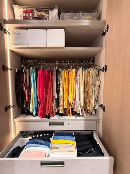 A pull-out drawer reveals neatly folded clothes, while colorful scarves and tops hang above.