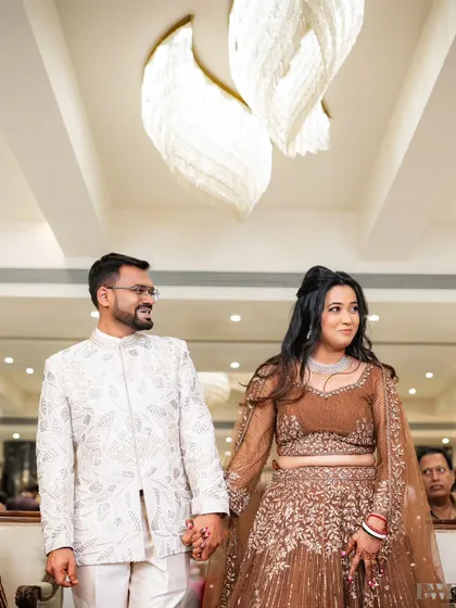 A candid shot of the couple walking hand-in-hand at their reception, with elegant chandeliers in the background adding a touch of luxury.
