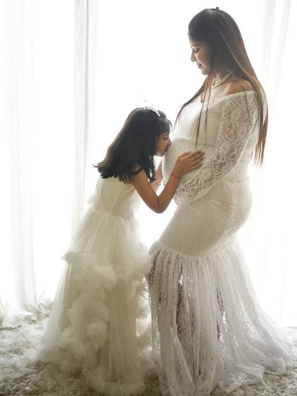 A daughter's kiss for her unborn sibling is a precious memory. This silhouette-style shot against a bright background is artistic and full of emotion.