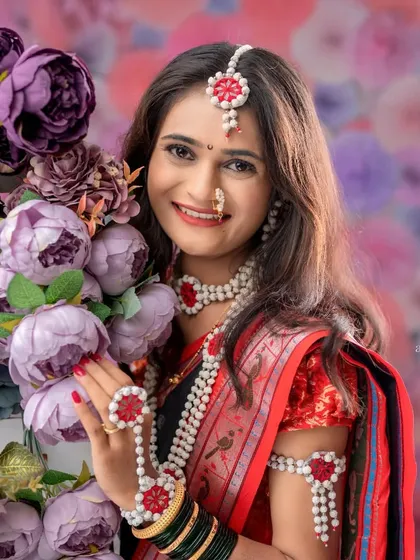 A stunning portrait of a woman adorned in halwyache dagine, posing with a bouquet of flowers. The floral background complements her festive look.