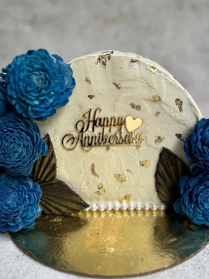 A beautiful top-forward cake for a wedding anniversary. This Belgian Chocolate cake is decorated with buttercream frosting, gold leaf, and stunning dried blue flowers for a modern yet elegant look.