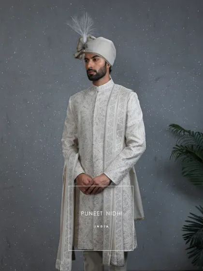 This complete ivory sherwani ensemble, with its matching stole and turban, blends historical opulence with modern sophistication. The detailed embroidery is designed for the groom who values cultural richness.