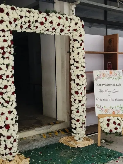 Even a simple entrance can be made beautiful. Here, I created a square arch using white and red flowers and placed a personalized "Happy Married Life" sign on an easel to welcome guests to the ceremony.