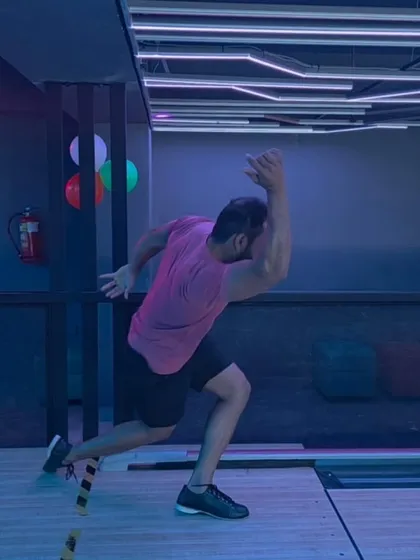 A player in mid-stride, showing the dynamic and athletic form of a serious bowler. The purple and blue lighting adds to the energetic vibe of our bowling alley.