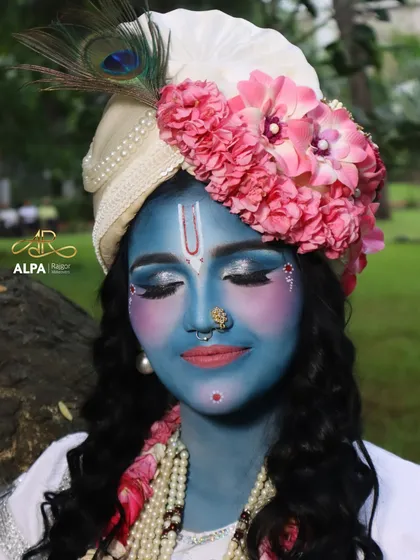 A close-up of the Krishna makeup. The look features a smooth blue base, serene eye makeup, and a floral-adorned turban with a peacock feather.