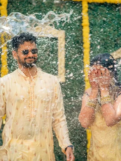 The Haldi ceremony is all about unrestrained joy. I love capturing these candid, fun-filled moments, like this one where the couple is showered with water against a vibrant backdrop of marigolds and a custom green wall.