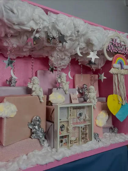 A wider view of the 'little angel' hamper, showing the personalized name sign, rainbow macrame, and the arrangement of gifts that create a whimsical sky scene.