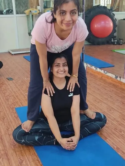 Smiles and support are a big part of our classes. This image captures the fun and encouraging atmosphere as one student helps another with a gentle back and shoulder opening.