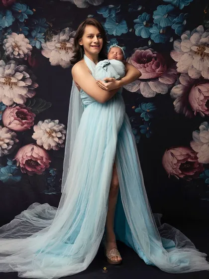 A stunning full-length portrait of a mother in a flowing blue gown, holding her newborn. This shot combines the elegance of maternity photography with the sweetness of a newborn session.