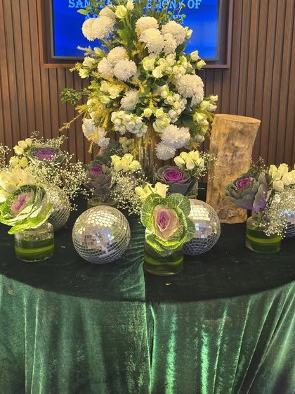 A unique table centerpiece combining white and purple flowers with mini disco balls on a green velvet tablecloth. This design mixes classic floral elements with a modern, playful twist.