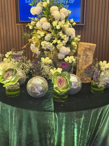 A unique table centerpiece combining white and purple flowers with mini disco balls on a green velvet tablecloth. This design mixes classic floral elements with a modern, playful twist.