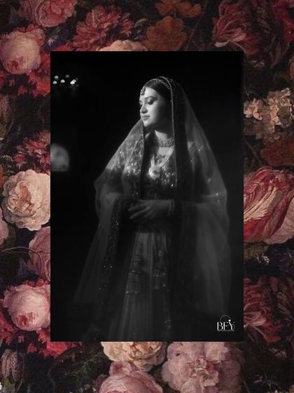 A moody black and white portrait of a bride under her veil, framed by a dark floral pattern.