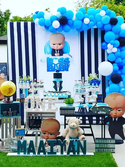 This outdoor Boss Baby setup shows how I can adapt themes for any space, even a garden. The decoration includes a classic black and white striped backdrop, character cutouts, and a full dessert table arrangement, making it perfect for a stylish first birthday.