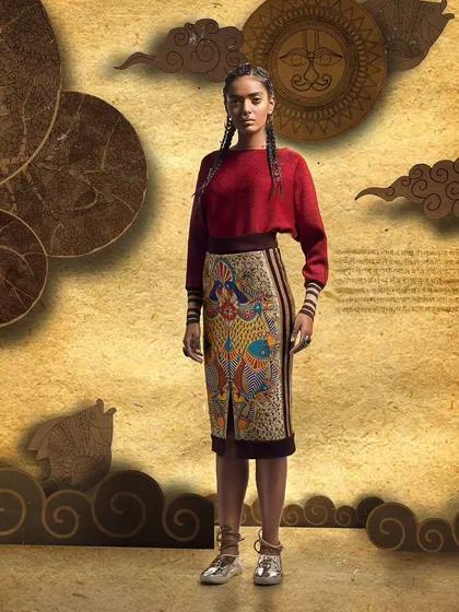 A straight-on look from a designer lookbook, featuring a pencil skirt with intricate traditional artwork. The simple styling emphasizes the detailed craftsmanship of the main garment.