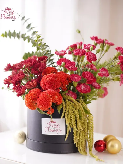 This 'Autumn Glow' arrangement captures warm tones with vibrant red celosia, mini carnations, and trailing amaranthus in a sleek black box. It's a bold and stylish choice for any celebration.