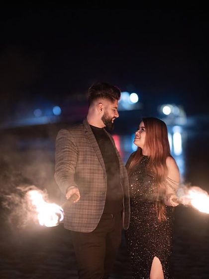 A striking color photo of the couple holding torches, with the fire illuminating them against the dark night, creating a powerful pre-wedding image.
