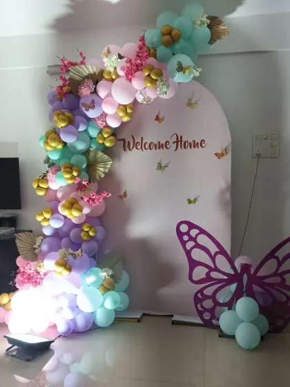 A whimsical butterfly-themed welcome home setup. The pastel rainbow balloon arch is decorated with gold butterflies and cherry blossoms, with a large butterfly cutout adding a beautiful touch to the arrangement.