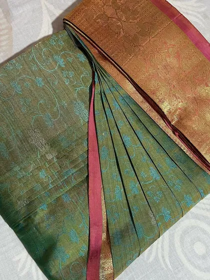 A lovely olive green saree with a pink border, folded and ready for storage.