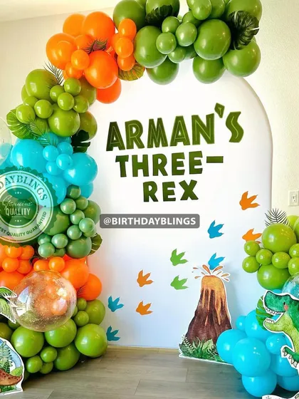 A "Three-Rex" dinosaur party with a vibrant balloon arch in green, orange, and blue. The volcano and dinosaur footprint details are a great touch.